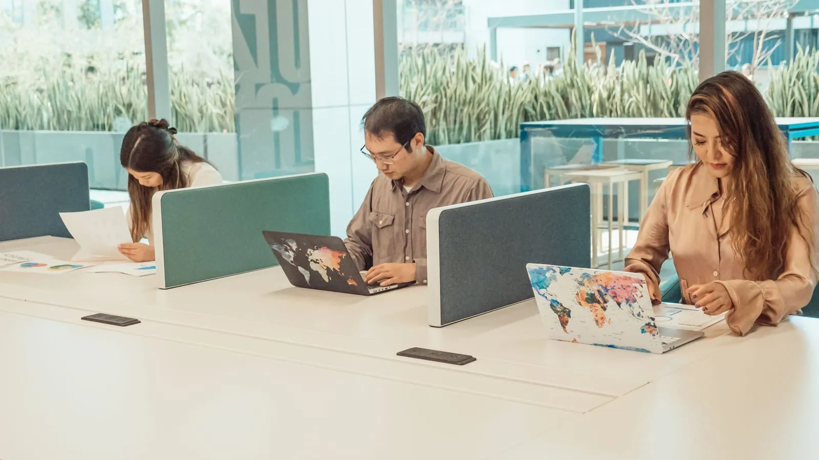 Three people working separately on laptops at shared desks in an open coworking space.